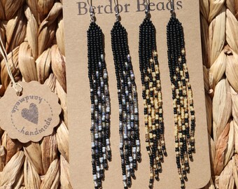 Pode incluir: Três pares de brincos de contas em um cartão com o texto "Berdor Beads". Os brincos são pretos, cinza e bege com um efeito degradê.