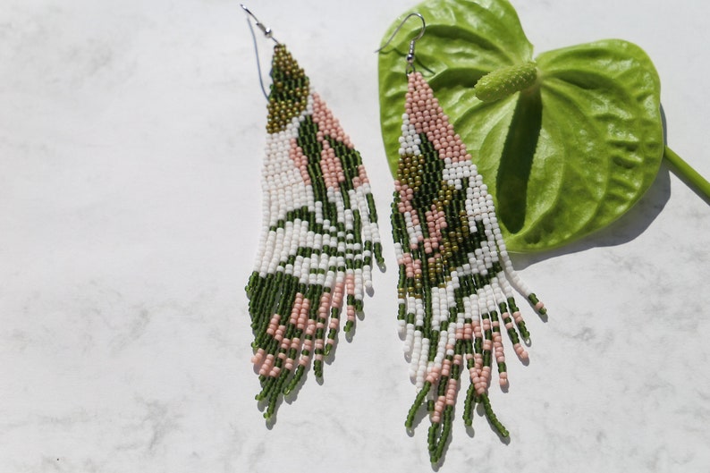 May include: A pair of long, beaded earrings with a geometric pattern in shades of green, white, and pink.