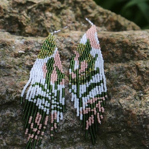 May include: A pair of long, beaded earrings with a geometric pattern in shades of green, white, and pink.