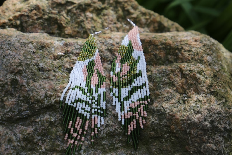 May include: A pair of long, beaded earrings with a geometric pattern in shades of green, white, and pink.