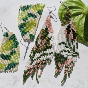 May include: Three pairs of long, beaded earrings in green, white, and pink. The earrings are made with small, colorful beads and have a fringe-like design.