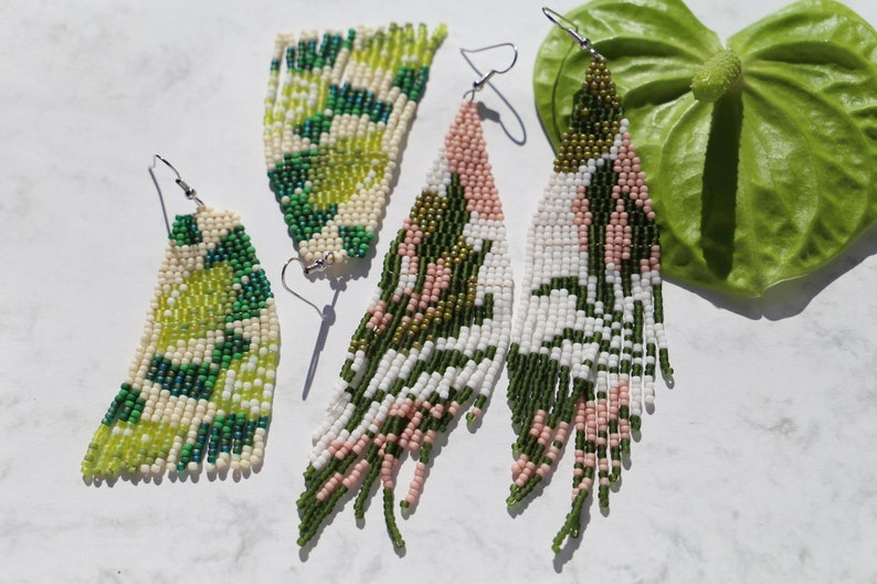 May include: Three pairs of long, beaded earrings in green, white, and pink. The earrings are made with small, colorful beads and have a fringe-like design.