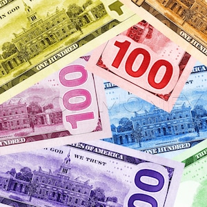 May include: A collection of overlapping United States one hundred dollar bills printed in various colors including yellow, pink, blue, and purple. Each bill features the text 100, Independence Hall, and the phrases In God We Trust and United States of America.