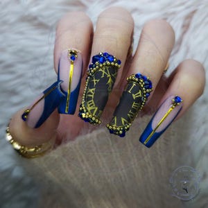 May include: Close-up of long, blue and gold nail art with a clock face design. The nails are decorated with rhinestones and gold accents.
