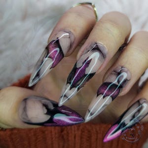 May include: Long, pointed acrylic nails with a dark purple and black bat-wing design. The nails have a clear base with a smoky effect, and the bat wings are outlined in white. The overall look is gothic and edgy.