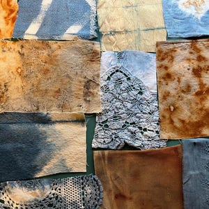 May include: A collection of rectangular fabric swatches featuring various textures and patterns. The pieces include natural-dyed brown and tan textiles, blue and white tie-dye prints, and intricate white and blue lace trim accents with frayed edges.
