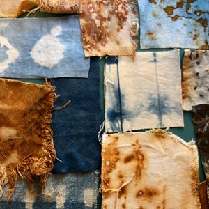 May include: A collection of rectangular fabric swatches featuring various textile techniques. The pieces display natural botanical prints, indigo blue tie-dye patterns, solid dark blue textures, and frayed edges on several of the woven materials.