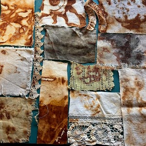 May include: A collection of rectangular fabric scraps featuring various tea-stained and rust-dyed patterns in shades of brown, tan, and cream. The assortment includes pieces of plain woven cloth with frayed edges alongside strips of intricate lace trim.