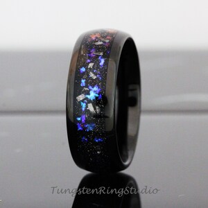 May include: A black tungsten ring with a blue, purple and orange glitter inlay. The ring is polished and has a bevelled edge.