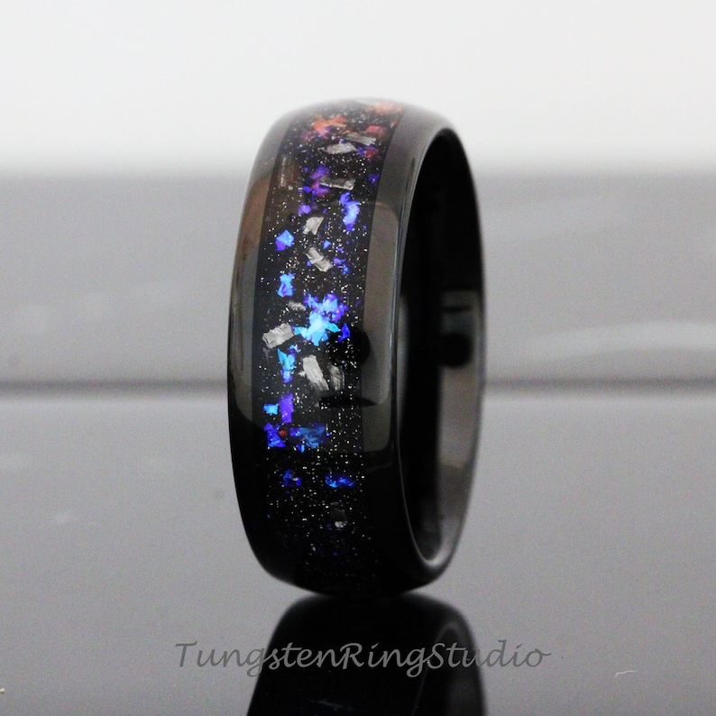 May include: A black tungsten ring with a blue, purple and orange glitter inlay. The ring is polished and has a bevelled edge.