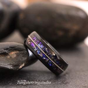 May include: A black tungsten carbide ring with a blue and purple inlay. The inlay has a textured, speckled appearance. The ring has a thin silver band running around the center.