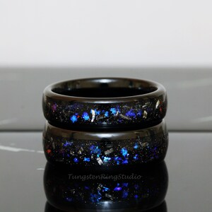 May include: Two black tungsten carbide rings with blue and silver glitter embedded in the black resin. The rings are stacked on top of each other.