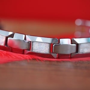 May include: A silver tungsten bracelet with white opal accents. The bracelet has a polished finish and is made of durable metal.