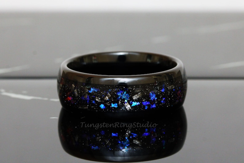 May include: Black tungsten ring with blue and silver glitter embedded in the band. The ring is polished and has a high shine.