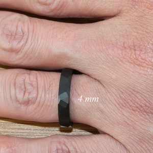May include: A black ring with a faceted design, worn on a finger. The ring is 4 mm wide.