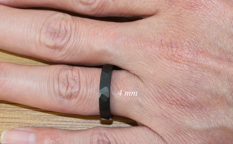 May include: A black ring with a faceted design, worn on a finger. The ring is 4 mm wide.