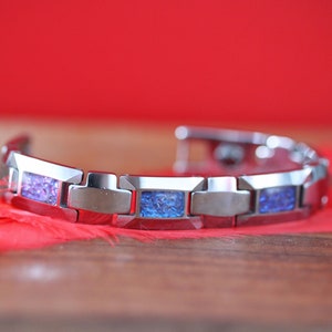 May include: A silver bracelet with blue and purple inlay. The bracelet has a magnetic clasp.