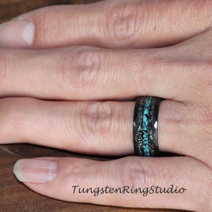 May include: A black tungsten ring with a turquoise inlay and a black carbon fiber band. The ring is worn on a person's finger.