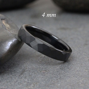 May include: A black tungsten carbide ring with a hammered finish. The ring is 4 mm wide.