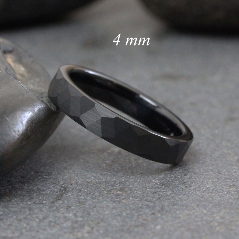 May include: A black tungsten carbide ring with a hammered finish. The ring is 4 mm wide.