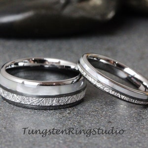 May include: Two silver tungsten wedding bands with a white inlay and a textured finish. The bands are on a gray surface. TungstenRingStudio.