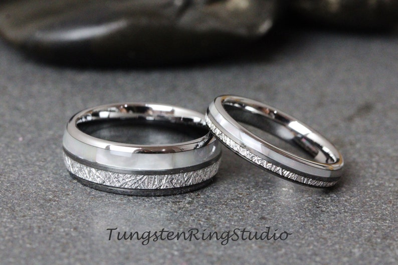 May include: Two silver tungsten wedding bands with a white inlay and a textured finish. The bands are on a gray surface. TungstenRingStudio.