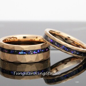 Op de afbeelding: Twee gouden ringen van wolfraamcarbide met een gehammerde afwerking en een zwarte inlay met iriserende blauwe en paarse glitter.