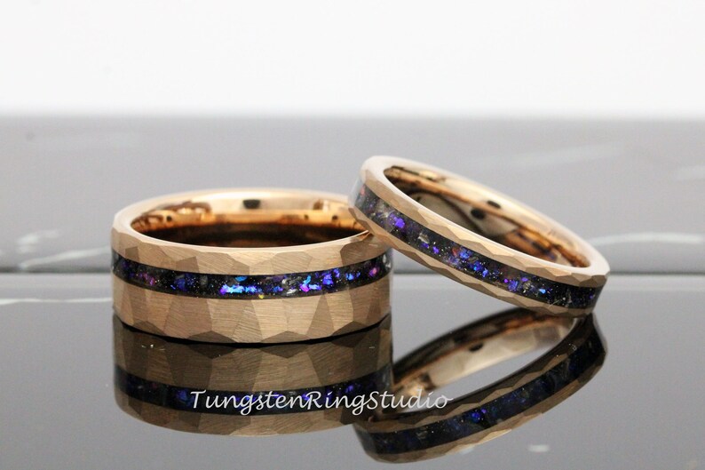 Op de afbeelding: Twee gouden ringen van wolfraamcarbide met een gehammerde afwerking en een zwarte inlay met iriserende blauwe en paarse glitter.