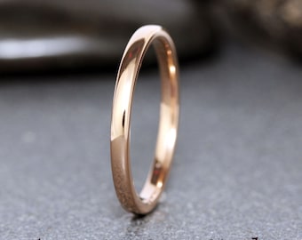 May include: A simple, polished rose gold tungsten carbide wedding band. The band is thin and has a smooth, rounded edge.