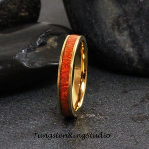 May include: A gold tungsten carbide ring with a thin band of orange opal inlay.