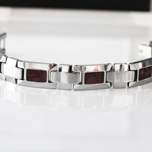 May include: A silver bracelet with brown inlay. The bracelet has a clasp closure.
