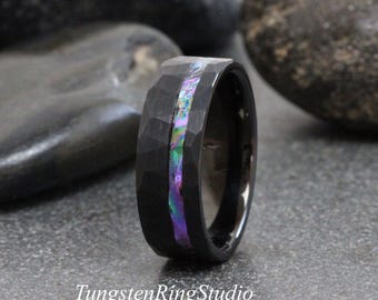 May include: Black tungsten ring with a hammered finish and an iridescent inlay of purple, green, and blue. The ring has a polished inner band. The text "TungstenRingStudio" is at the bottom.