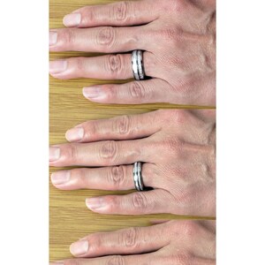 May include: Three tungsten carbide rings with a silver inlay. The rings are shown on a hand, with the top ring being 4mm wide, the middle ring being 6mm wide, and the bottom ring being 8mm wide.