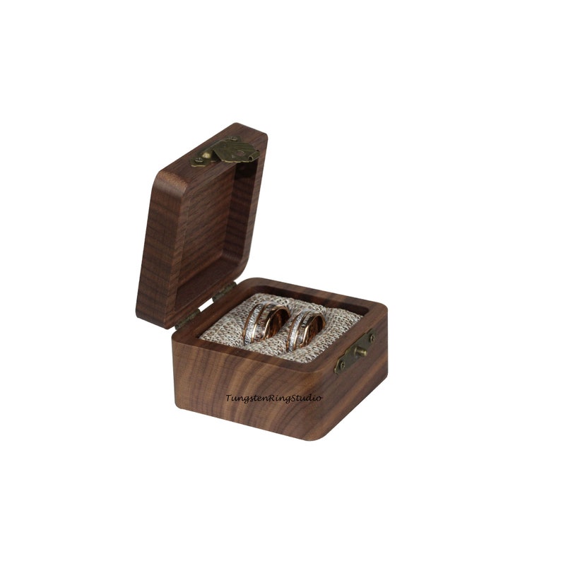 Pu&ograve; includere: Una scatola di legno per anelli con un coperchio incernierato e una chiusura in ottone. La scatola &egrave; aperta e all'interno ci sono due anelli d'oro e d'argento. La scatola &egrave; foderata con un tessuto beige.