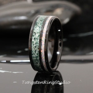 May include: A black tungsten ring with a green and white inlay. The ring has a polished finish and a beveled edge.