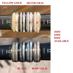 May include: Four different colored men's wedding bands with a white inlay. The bands are yellow gold, silver gray, black, and rose gold. The bands are 4mm, 6mm, and 8mm wide.  The text "4MM 6MM 8MM AVAILABLE" is printed below the bands.
