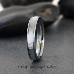May include: A silver tungsten ring with a white inlay. The ring is polished and has a beveled edge.