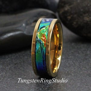 Könnte beinhalten: Ein goldfarbener Ring mit einem lebendigen, schillernden Inlay in Blau-, Grün- und Rottönen. Der Ring hat eine polierte Oberfläche und der Text "TungstenRingStudio" ist unten sichtbar. Dieser Ring ist ein Schmuckstück.