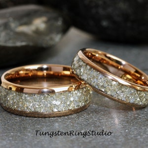 May include: Two rose gold rings, each featuring a band of sparkling, light-coloured stones. The rings are displayed on a grey surface, with the text "TungstenRingStudio" visible in the image.