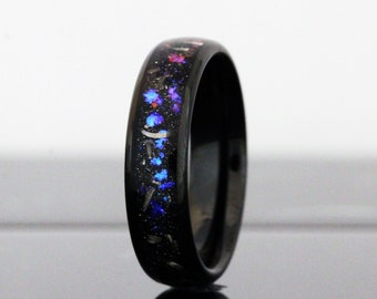 May include: A black ring with a band of sparkling blue, purple, and red embedded material. The ring has a polished finish and the text "TungstenRingStudio" is visible at the bottom.