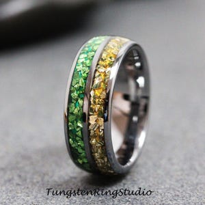 Puede incluir: Primer plano de un anillo plateado con incrustaciones verdes y doradas. El anillo tiene un acabado pulido y el texto "TungstenRingStudio" es visible en la parte inferior de la imagen.