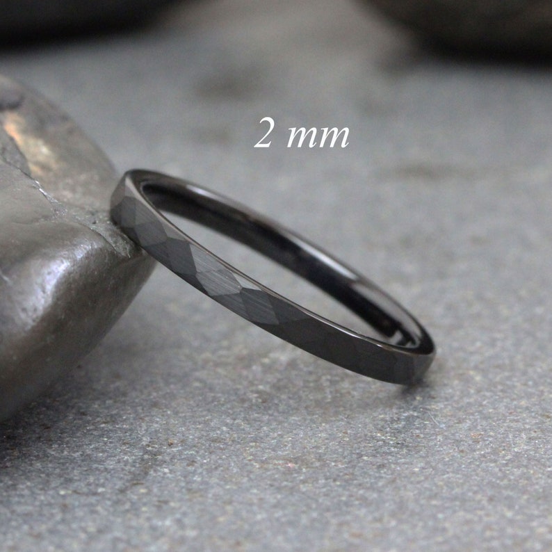 May include: A black, 2 mm wide, faceted tungsten carbide ring. The ring is shown on a grey, textured surface.