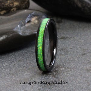 Op de afbeelding: Een zwarte ring van wolfraam met een groene opaal inlay. De ring is gepolijst en heeft een afgeschuinde rand.