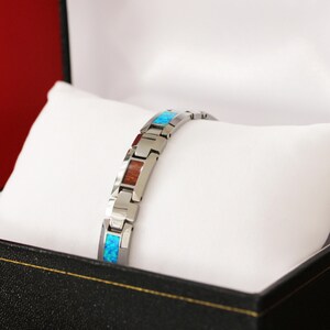 May include: A silver-toned bracelet with rectangular inlays of blue opal and reddish-brown wood, presented in a black jewelry box with a white pillow. The bracelet is made of linked metal segments.