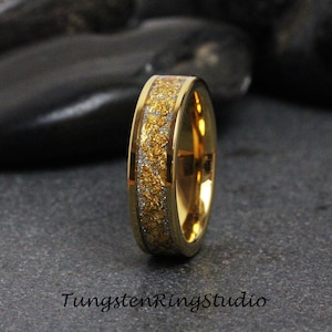 Puede incluir: Un anillo de carburo de tungsteno dorado con una incrustación de plata y oro. El anillo tiene un acabado pulido y un ajuste cómodo.