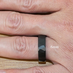 May include: A black ring with a hammered finish, worn on a finger. The ring is 6mm wide.