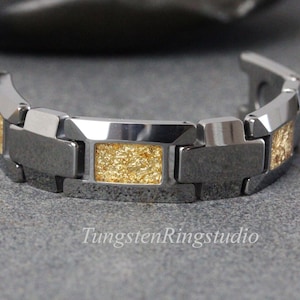 May include: A silver-toned bracelet with rectangular gold-colored inlays. The bracelet is made of a series of connected rectangular links. The text "TungstenRingstudio" is visible on the surface.
