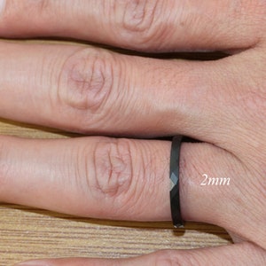 May include: A black ring with a diamond-shaped design on a finger. The ring is 2mm wide.