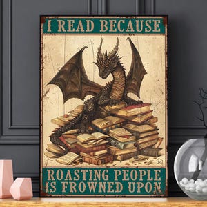 May include: A framed print featuring a dragon atop a stack of books. The text at the top reads "I READ BECAUSE" and the text at the bottom reads "ROASTING PEOPLE IS FROWNED UPON". The dragon is dark brown with large wings.
