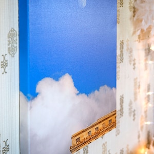 Pode incluir: Uma impress&atilde;o em tela de um edif&iacute;cio com um c&eacute;u azul e nuvens brancas. O edif&iacute;cio est&aacute; parcialmente obscurecido pelas nuvens.